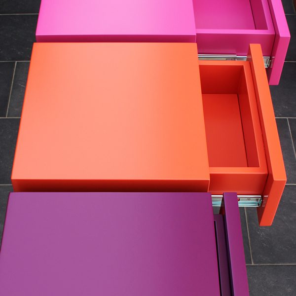 Console moderne décorative avec 3 tiroirs sur mesure à ouverture en façade. Console Pied-Estal avec un piétement en inox brossé. Tiroirs en couleurs finition laque contemporaine satinée, couleurs aubergine, orange pop, fuchsia. Photo détail tiroirs ouverts