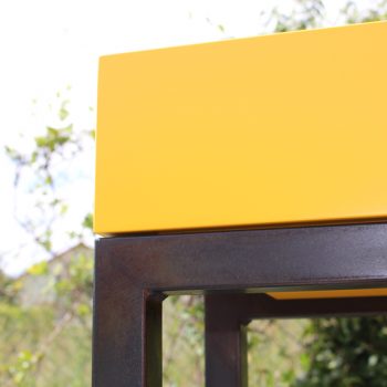 Console design sur-mesure, zoom sur le pied en acier patiné noi bruni de la console et le cube laqué de couleur jaune soleil intense. Mobilier Les Pieds Sur La Table créateur et fabricant de meubles contemporains design sur mesure.